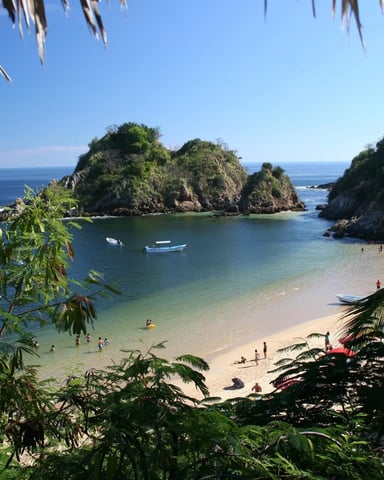Tropical beach cove with sandy shore, turquoise water, palm fronds, rocky islands, and boats anchored offshore