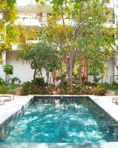 Courtyard with rectangular pool, lounge chairs, mature trees, and white multi-story building surrounding the space