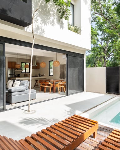 Modern house with pool, wooden lounge chairs, and open-plan interior visible through large glass doors