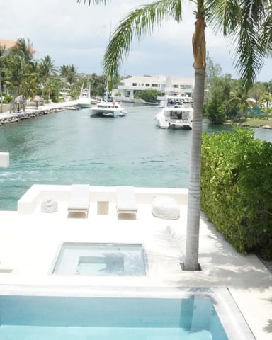 Waterfront villa with pool overlooking turquoise lagoon, moored boats, and white buildings among palm trees
