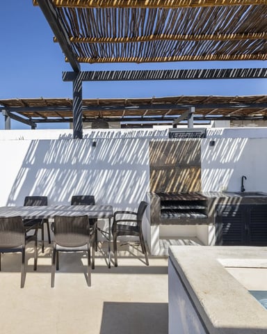 Rooftop terrace with dining table, chairs, pergola shade, built-in grill, and pool edge under clear blue sky