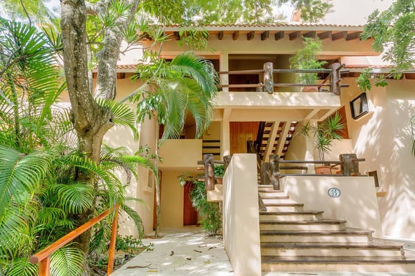 Mesa de comedor en el patio con cubiertos y frutero, con vistas a una piscina rectangular, enredaderas floridas y montañas